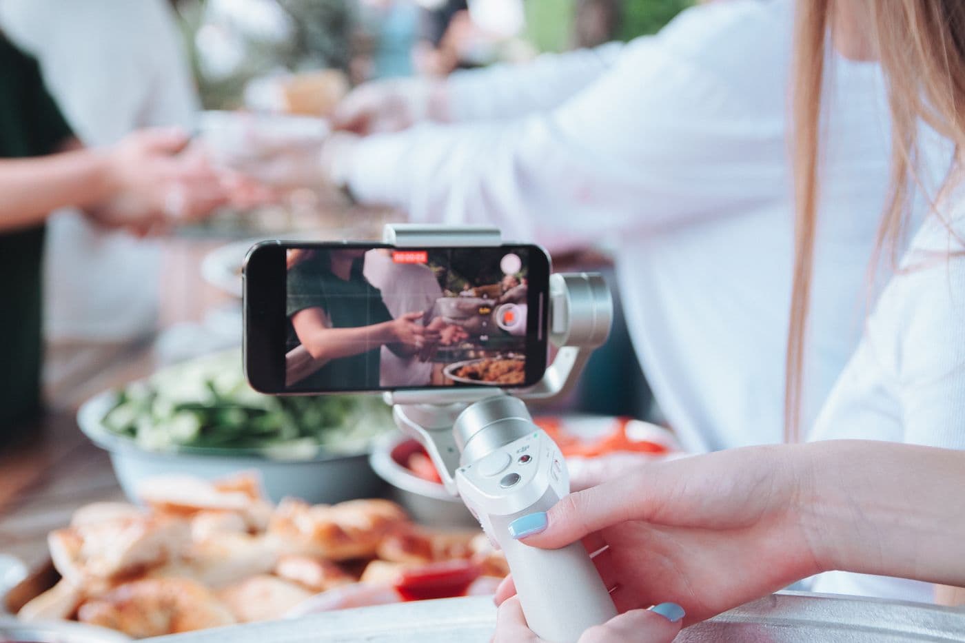 A person filming a food event with a smartphone gimbal