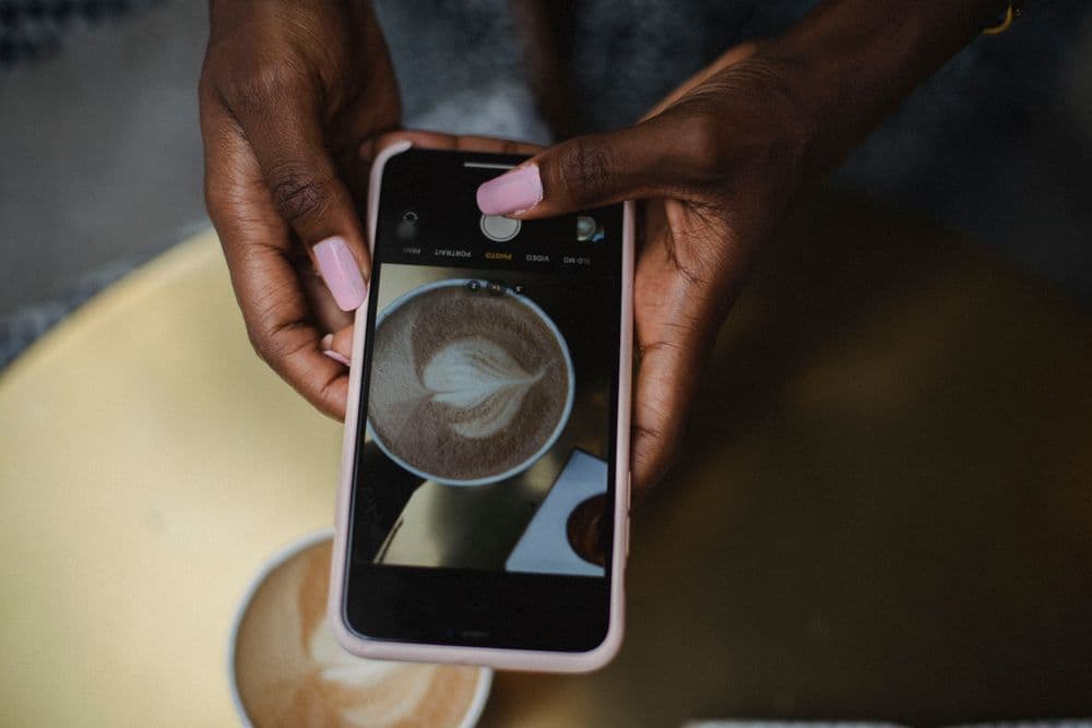 Hands photographing a latte with a phone